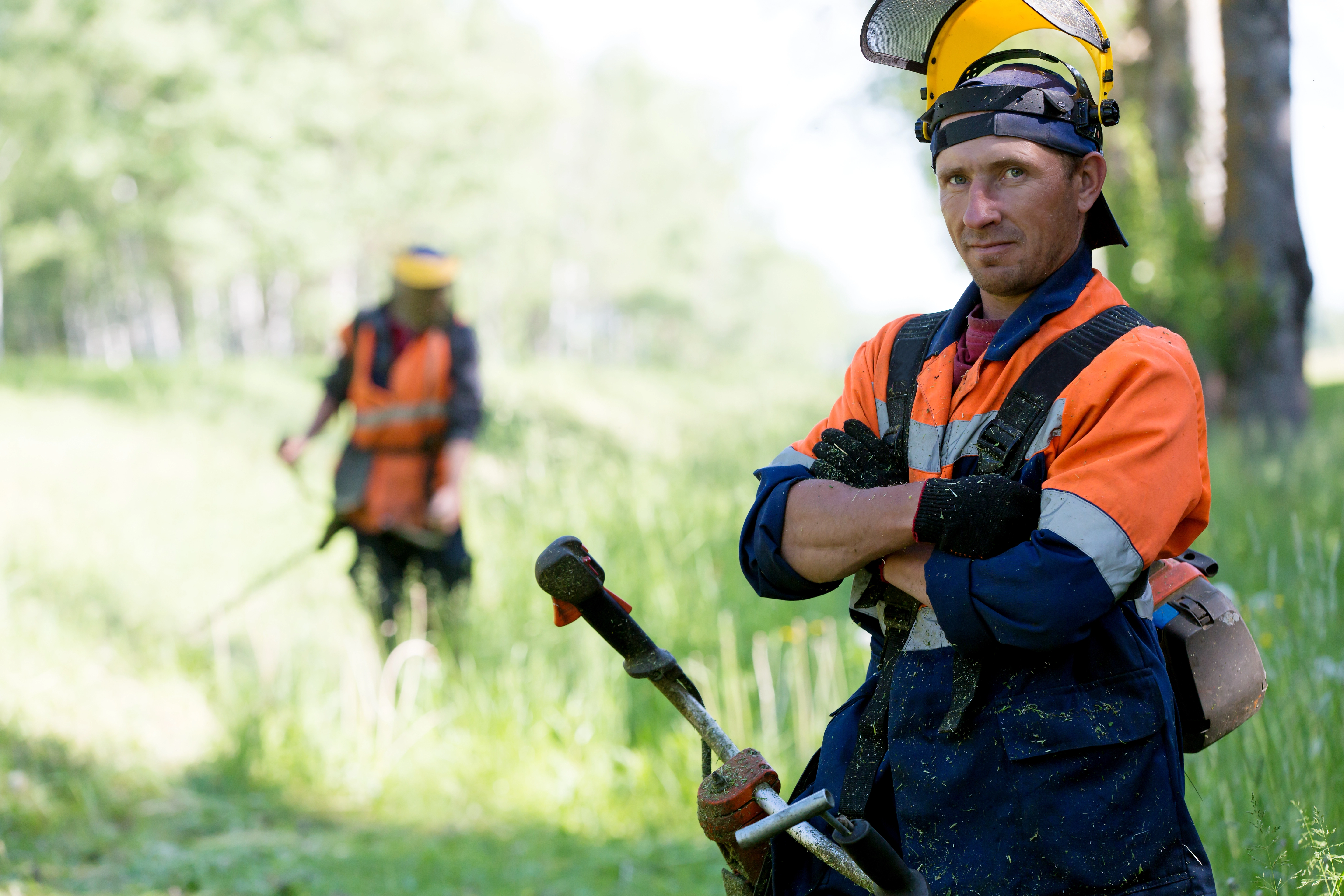 Two people wearing hi-vis PPE using strimmers outside in a green space on a HSS Training Groundcare course